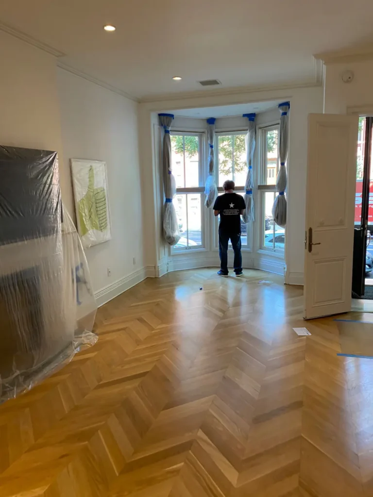 Brooklyn brownstone front parlor with bay windows, chevron wood floor, and protected finishes
