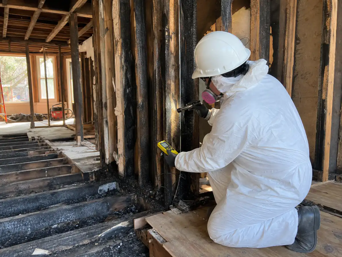 Restoration contractor assessing smoke-damaged framing and floor joists after a residential fire