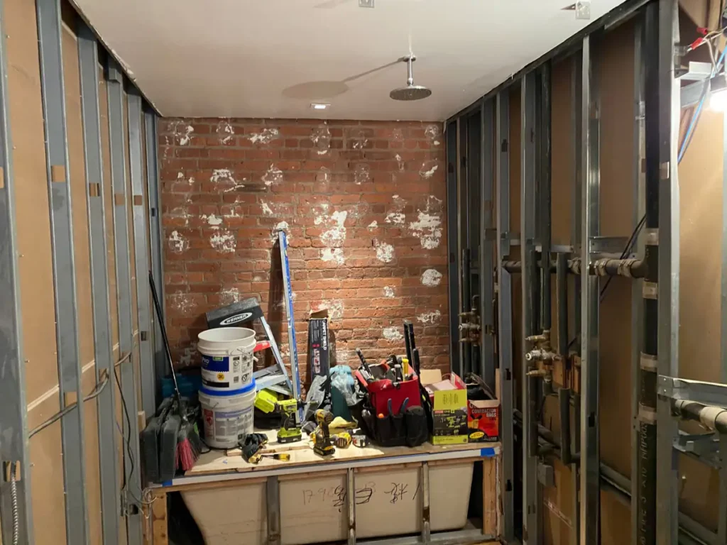 Bathroom walls opened to expose plumbing and framing during a Long Island City violation correction