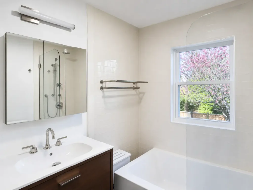 Wood vanity, tiled walls, bathtub, and frameless glass panel in the completed post-fire bathroom