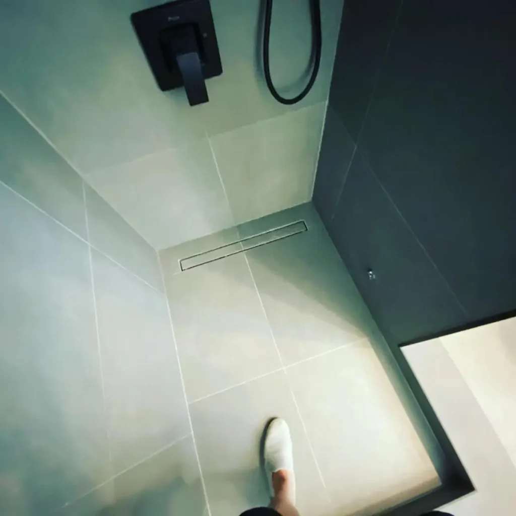 Large-format shower tile with slim linear drain and matte-black shower fixtures
