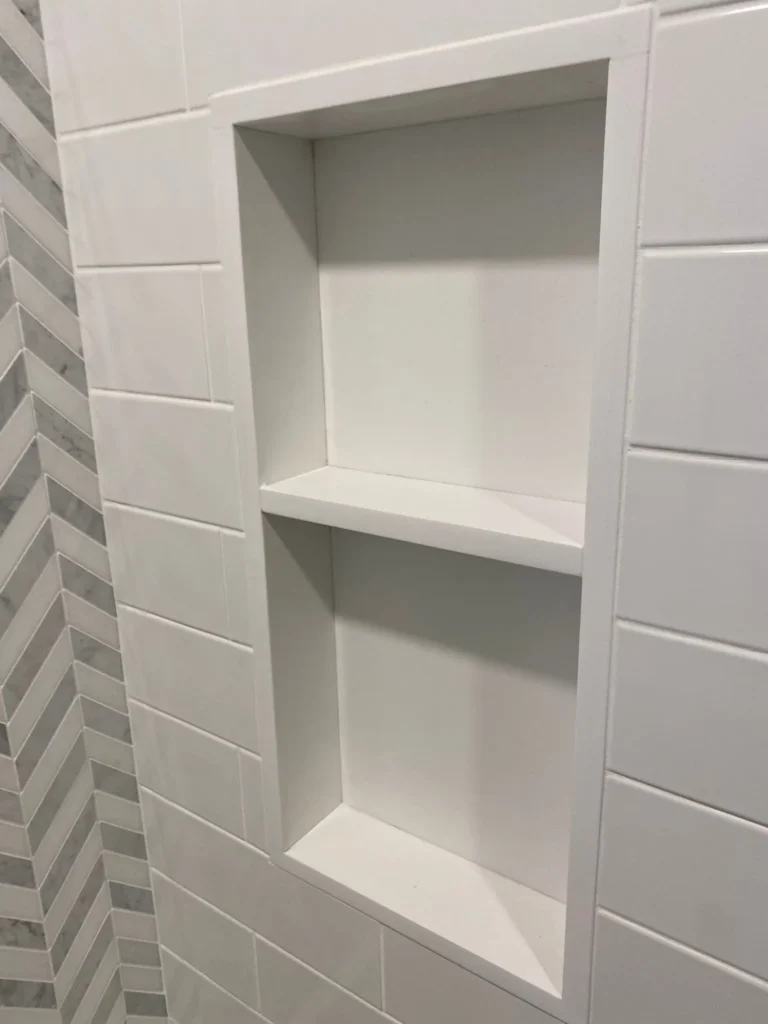 Two-level recessed shower niche framed by white subway tile and marble-look chevron accent tile in a Downtown Brooklyn renovation