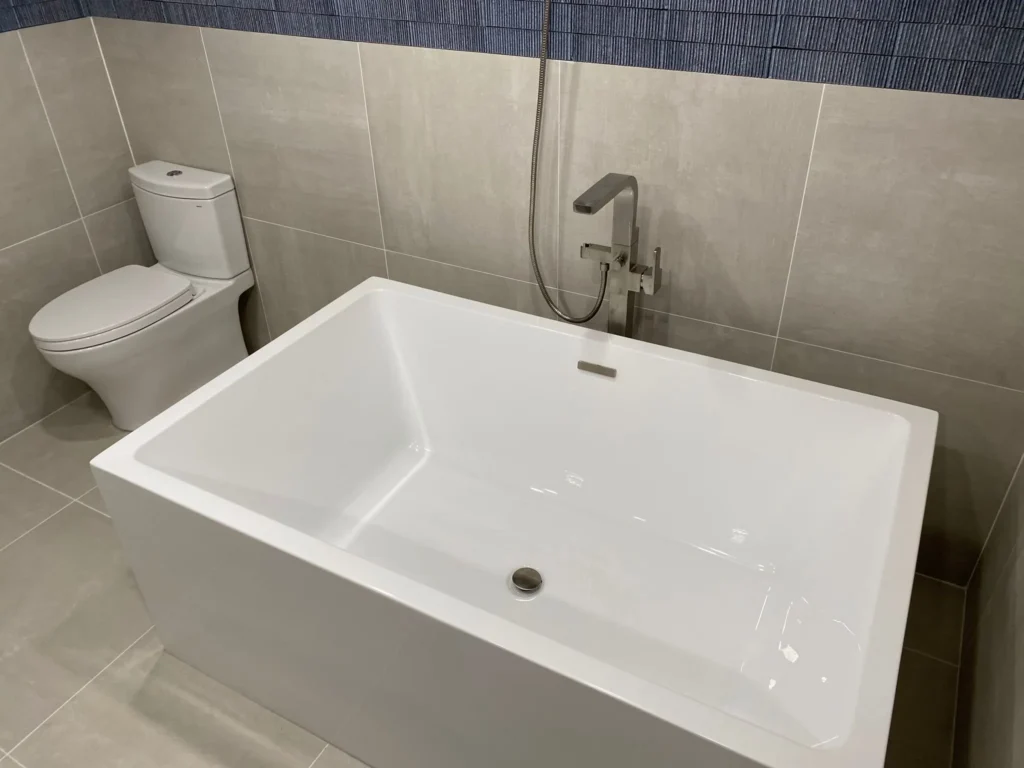 White freestanding tub with modern filler, handheld shower, gray porcelain tile, and deep-blue feature tile in a Park Slope bathroom renovation