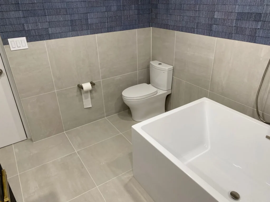 Rectangular freestanding bathtub and one-piece toilet surrounded by large warm-gray porcelain tile in a renovated Park Slope bathroom