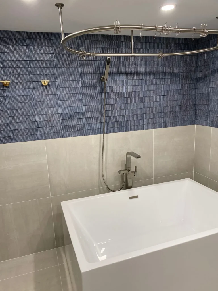 Freestanding tub with handheld shower and ceiling-mounted oval curtain track against deep-blue textured tile in Park Slope