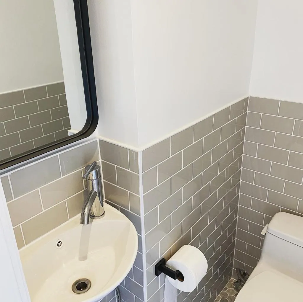 Gray subway-tile wainscot, black-framed mirror, chrome faucet, and compact corner sink in a Williamsburg half bath